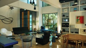 Un amplio salón con un ventanal grande, un sofá negro, una silla de vidrio y una mesa de comedor de madera.