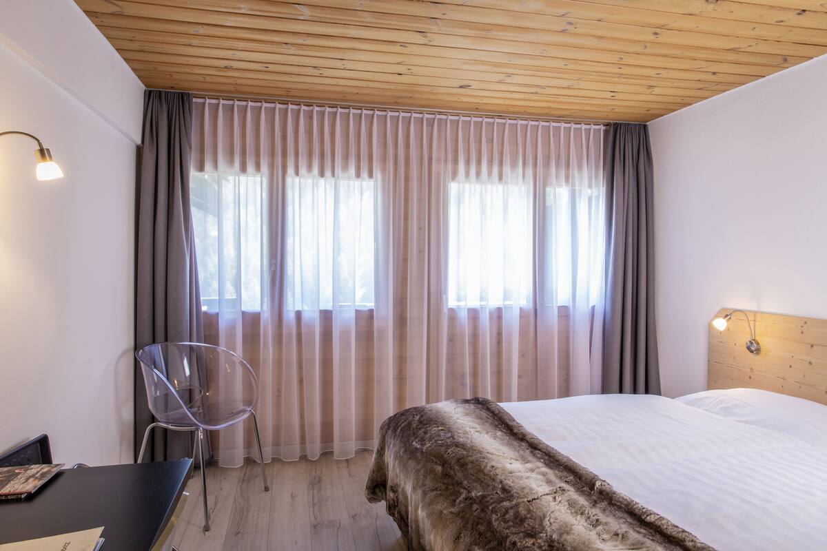 A hotel room with a bed, a desk, a chair, and a window with curtains.