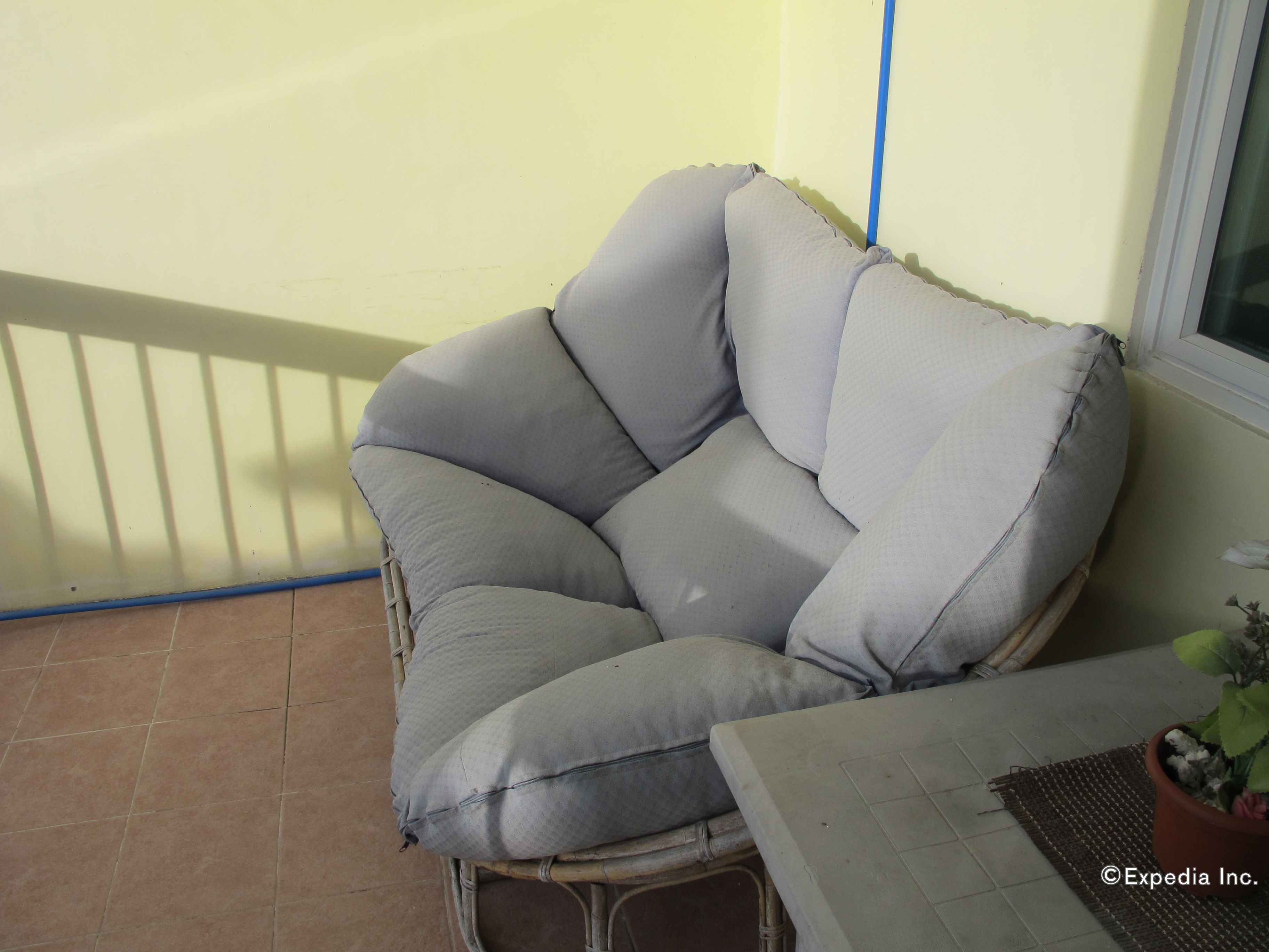 A wicker chair with grey cushions on a balcony.