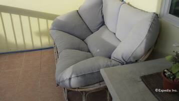 A wicker chair with grey cushions on a balcony.