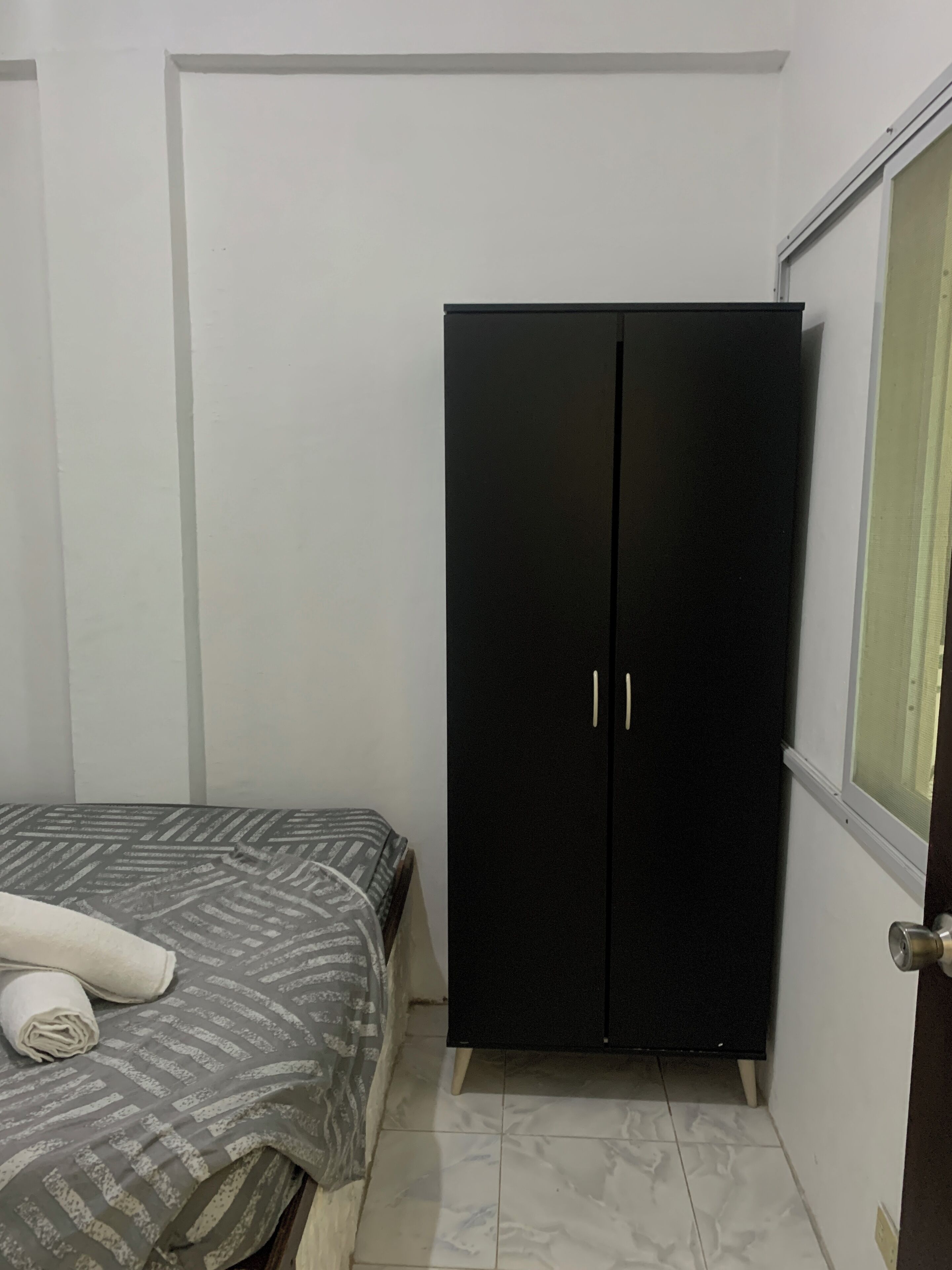 A bedroom with a bed, a black wardrobe, and a window.