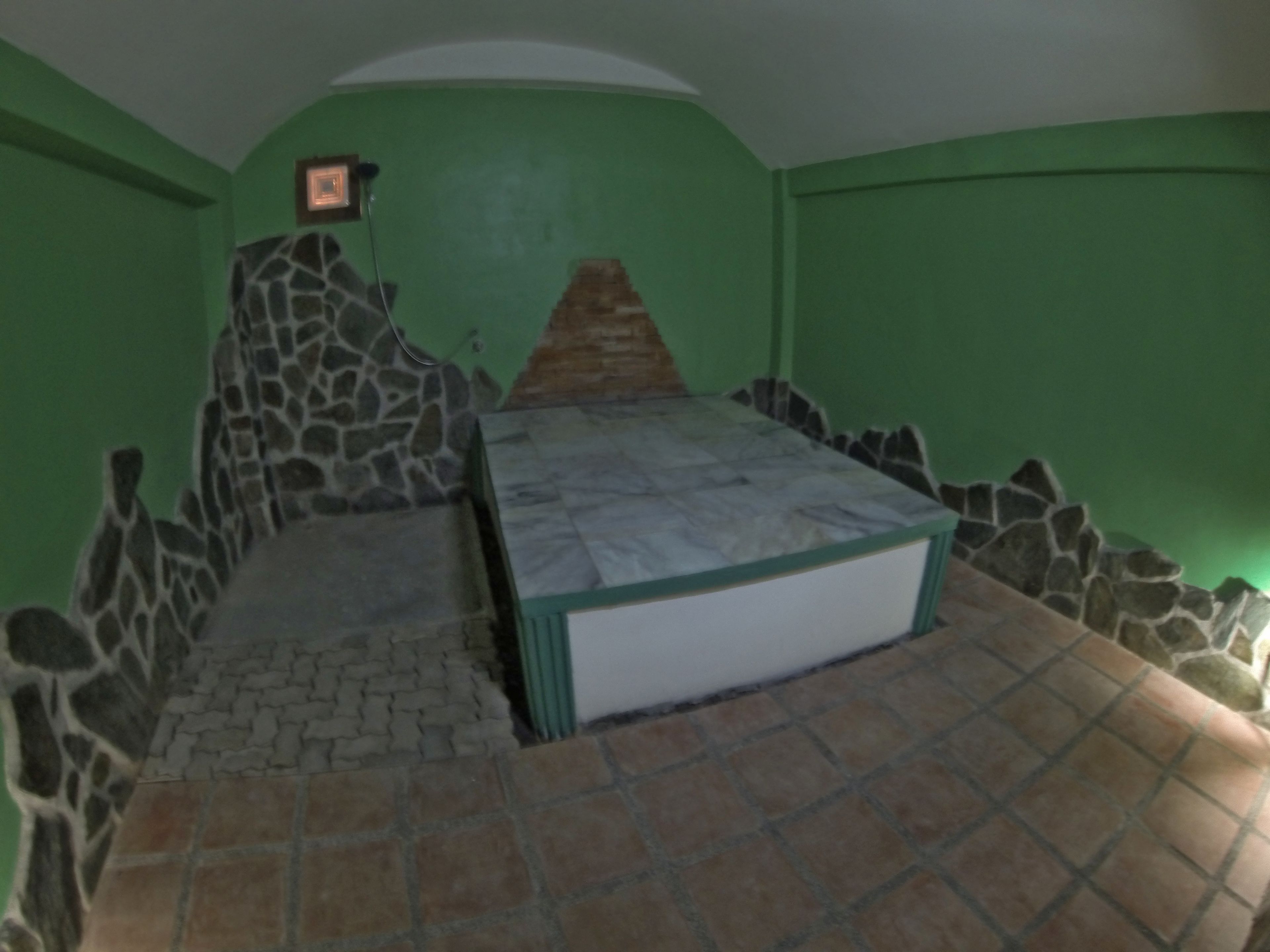 Una habitación con pared de piedra, cama con estructura verde y un cuadro pequeño en la pared.