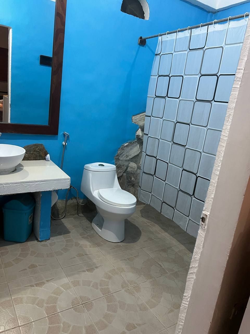 Un baño con pared azul, lavamanos blanco, inodoro y zona de ducha.