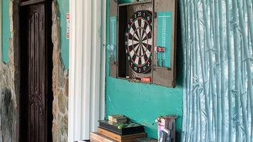 A room with a dartboard on the wall, a door, and a table with books and a plant.