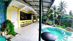 A covered outdoor area with a pool, seating, and a view of palm trees. - Dream Hill Condos & Spa (Puerto Galera)