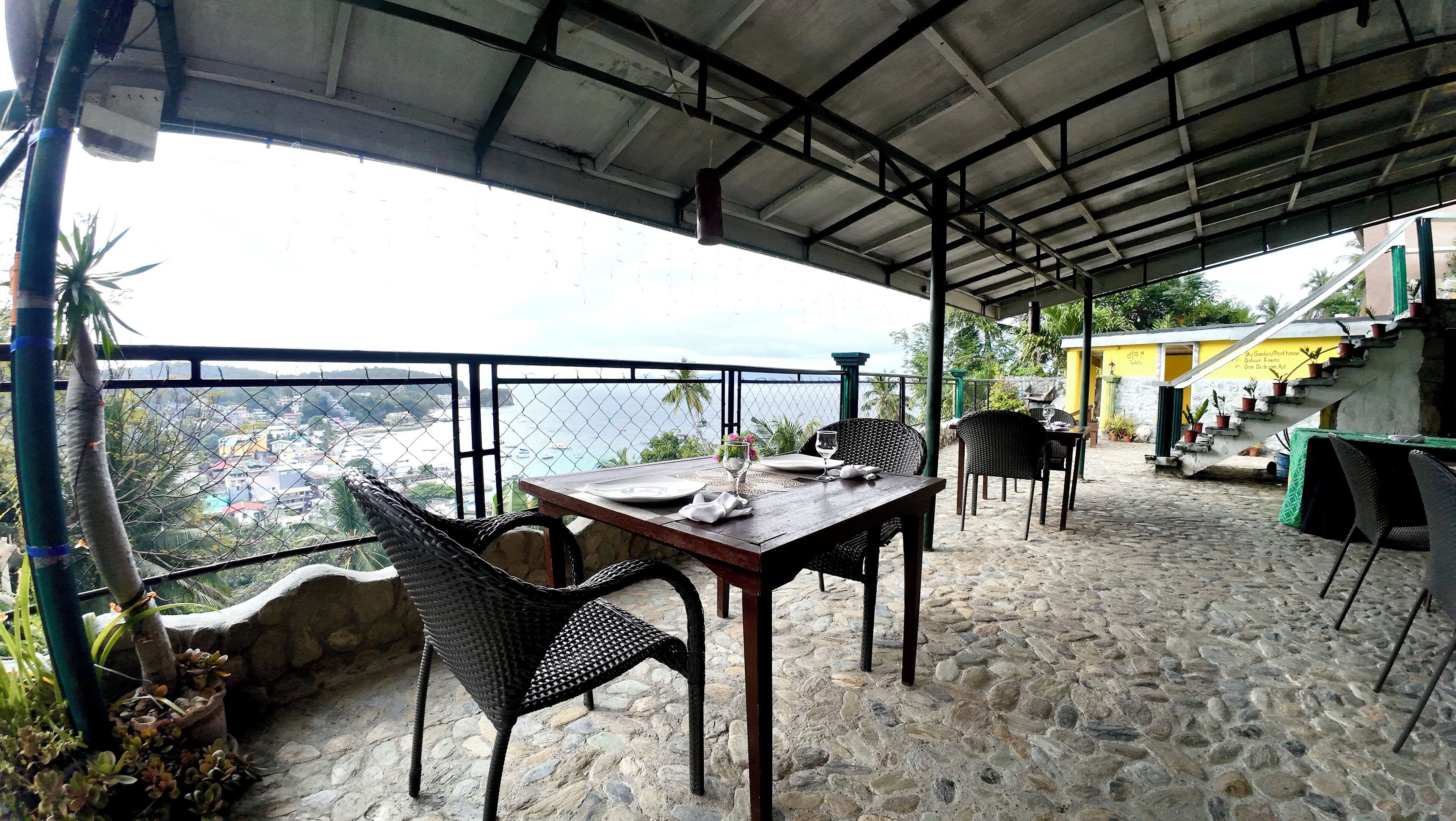 Un área de comedor al aire libre con una mesa para dos, sillas de mimbre y vista al océano.