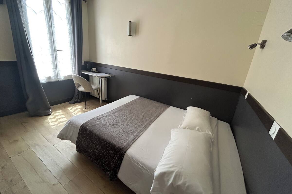 A hotel room with a bed, a desk, a chair, and a window with curtains.