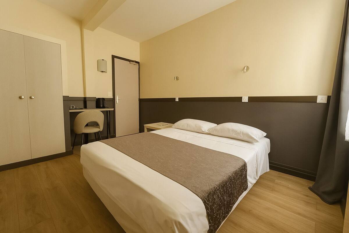 A hotel room with a bed, a desk, a chair, and a wardrobe.