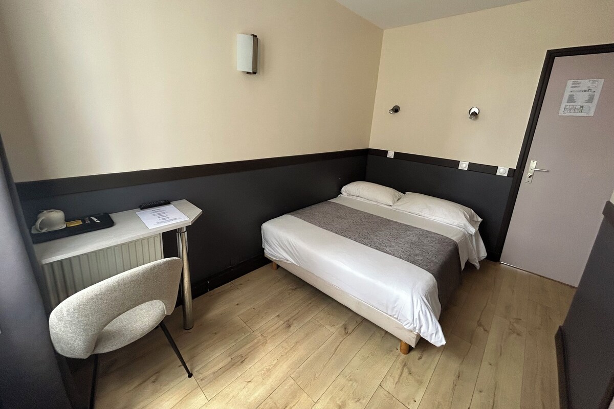 A small hotel room with a bed, a desk, a chair, and a door.
