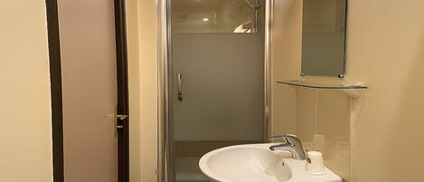 A bathroom with a glass-enclosed shower, a white sink with a mirror above it, and a glass shelf.