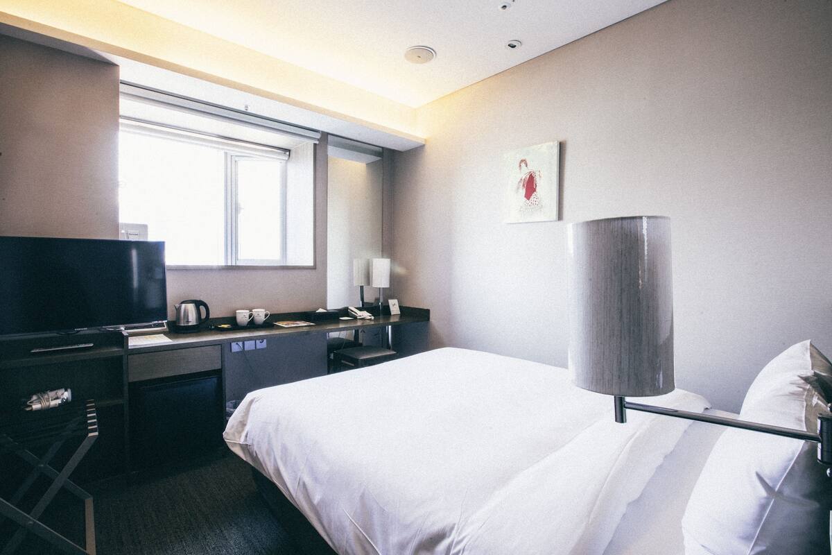 A hotel room with a bed, desk, and a television.