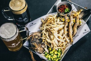 Una bandeja con pescado frito, un tazón de chili y dos jarras de cerveza sobre una mesa.