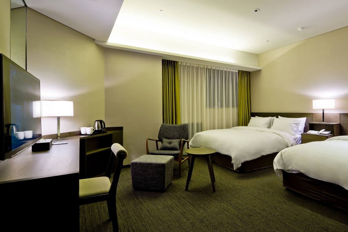 A hotel room with a bed, a desk, a chair, a small table, and a mirror.