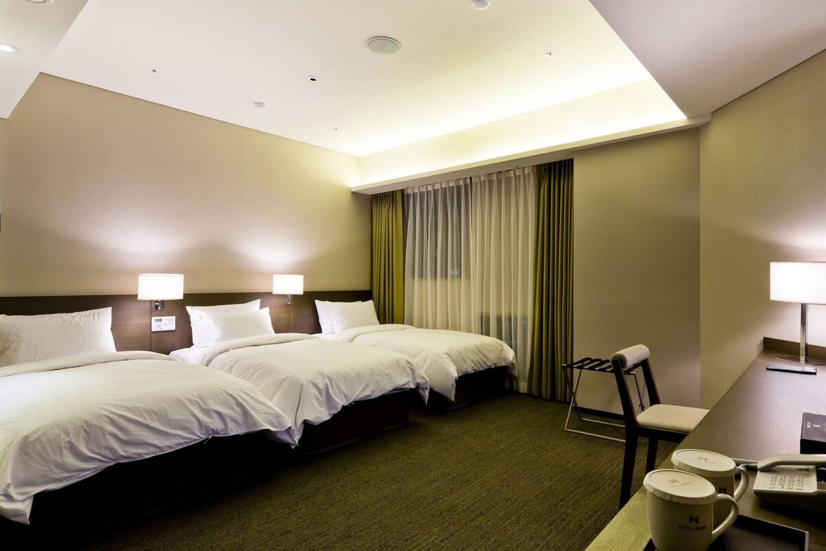 A hotel room with two beds, a desk with a telephone, and a chair.