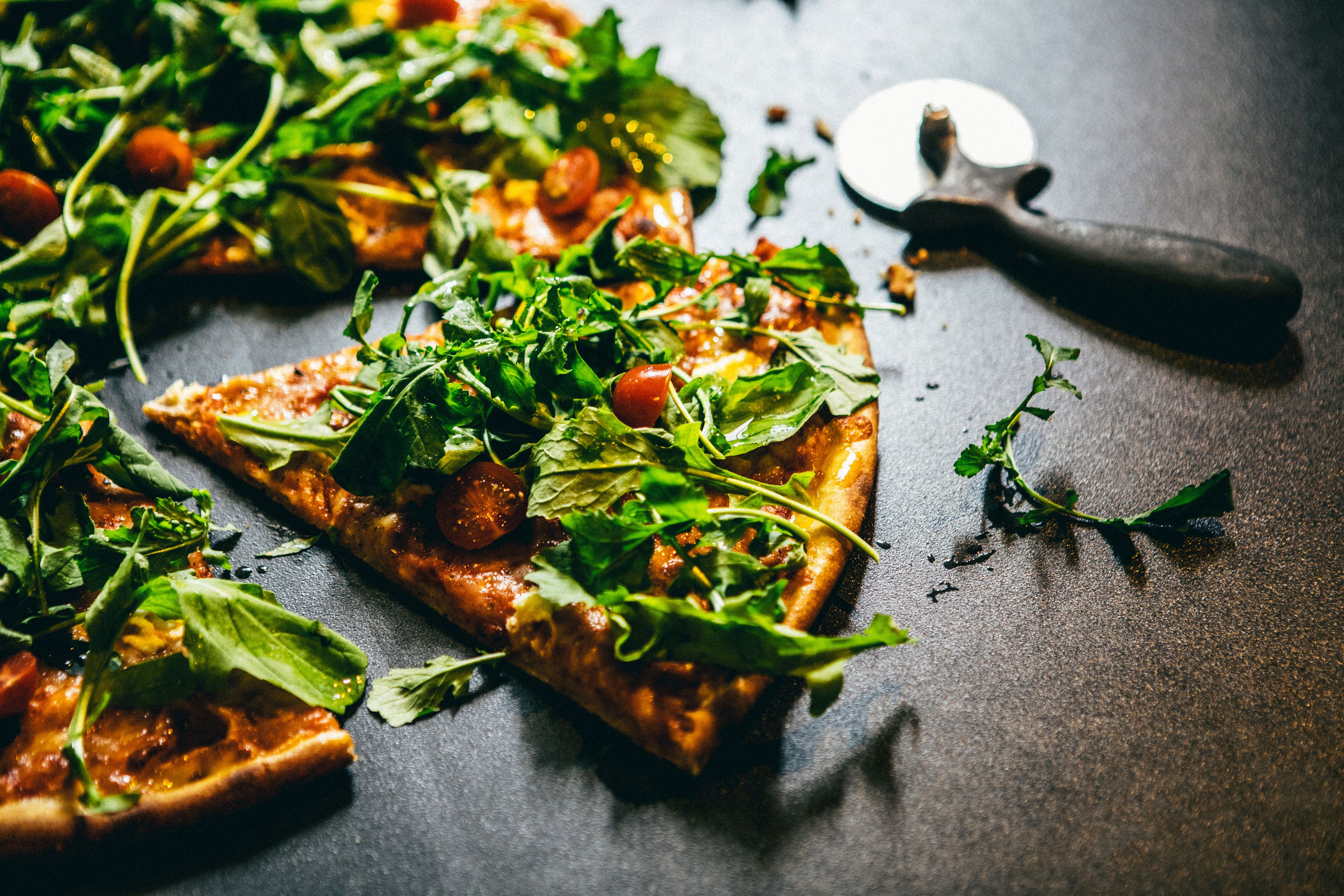 Una pizza con vegetales frescos y tomates sobre una superficie oscura.