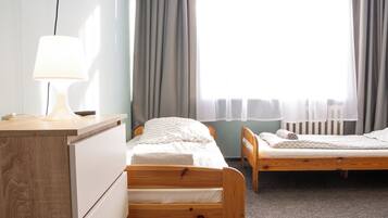 A room with two wooden beds, a desk with a lamp, a television on the wall, and a window with curtains.