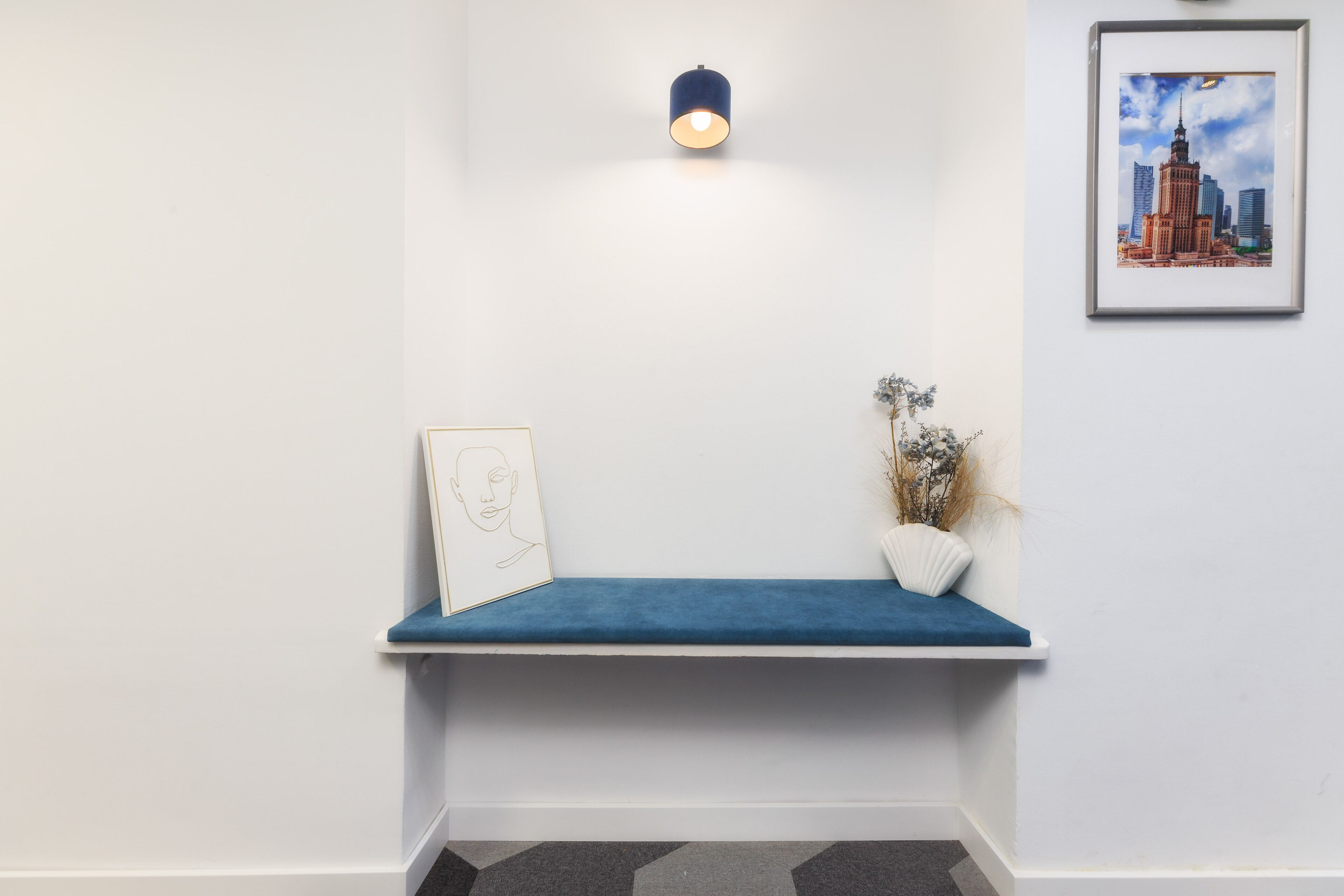 A hallway with a blue bench, a framed picture, a wall-mounted light, and a framed cityscape picture.