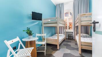 A room with three bunk beds, a television, a small round table with a potted plant, and a white chair.