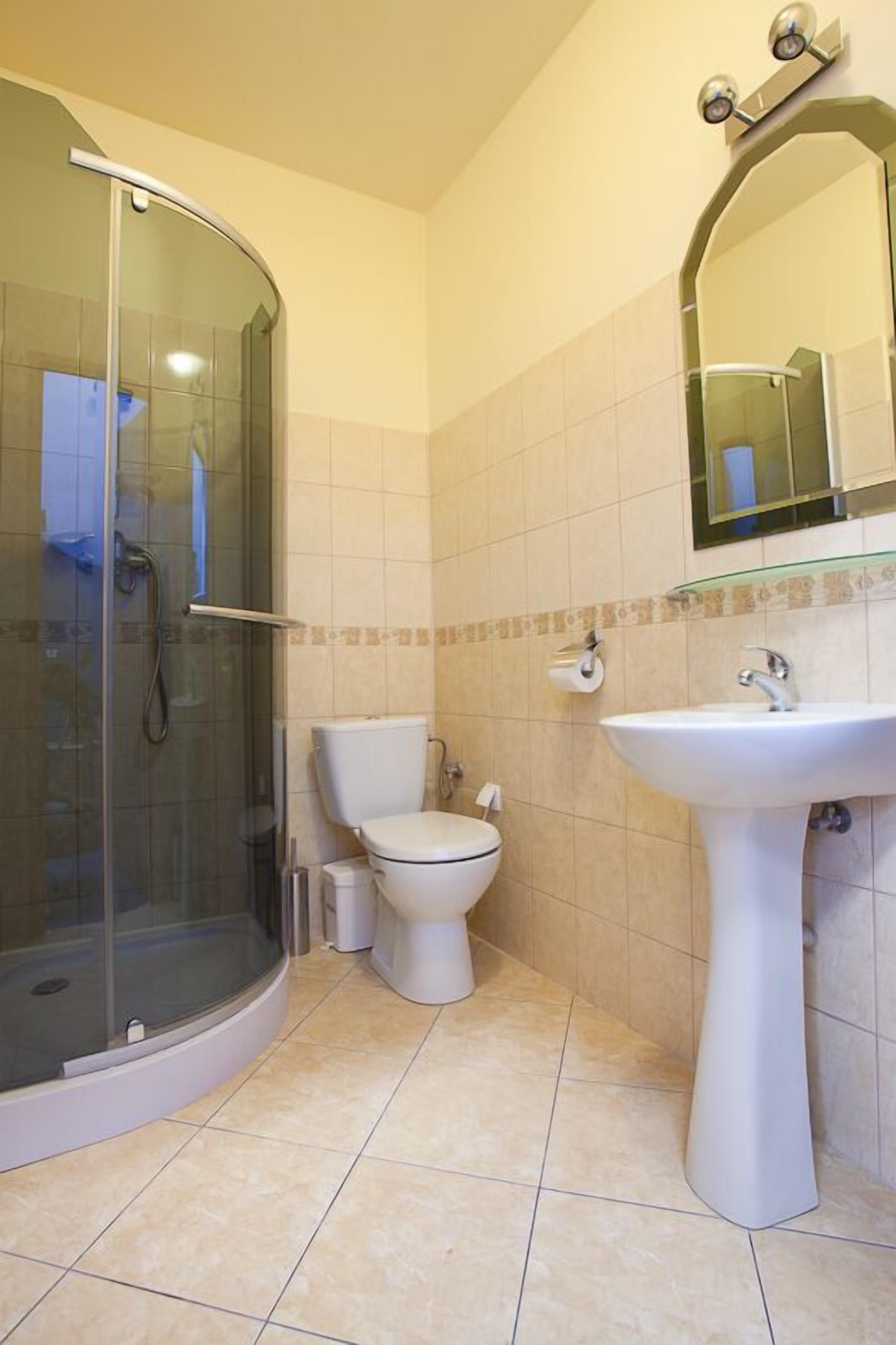 Ein Badezimmer mit Duschkabine aus Glas, Toilette und Waschbecken auf Säule.