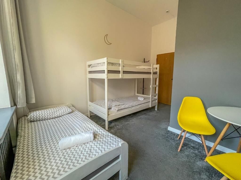 A room with a bunk bed, a small table, and two yellow chairs.