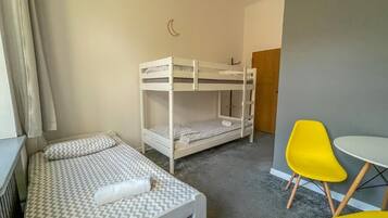 A room with a bunk bed, a small table, and two yellow chairs.