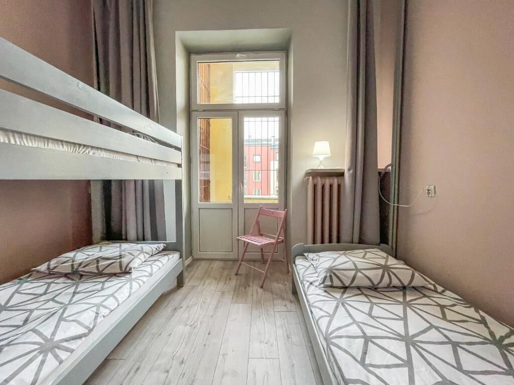 A small, compact room with two single beds, a chair, a window with curtains, and a radiator.