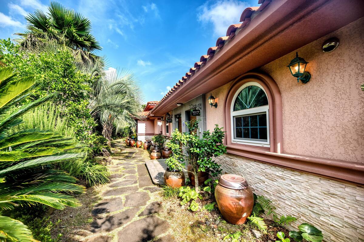 A pathway lined with potted plants and a building with a tiled roof and arched windows.