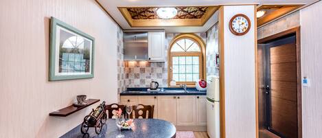 A compact kitchen with a round dining table, wooden cabinets, and a clock on the wall.