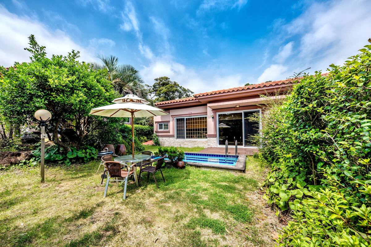 A backyard with a swimming pool, patio furniture, and a house with a tiled roof.