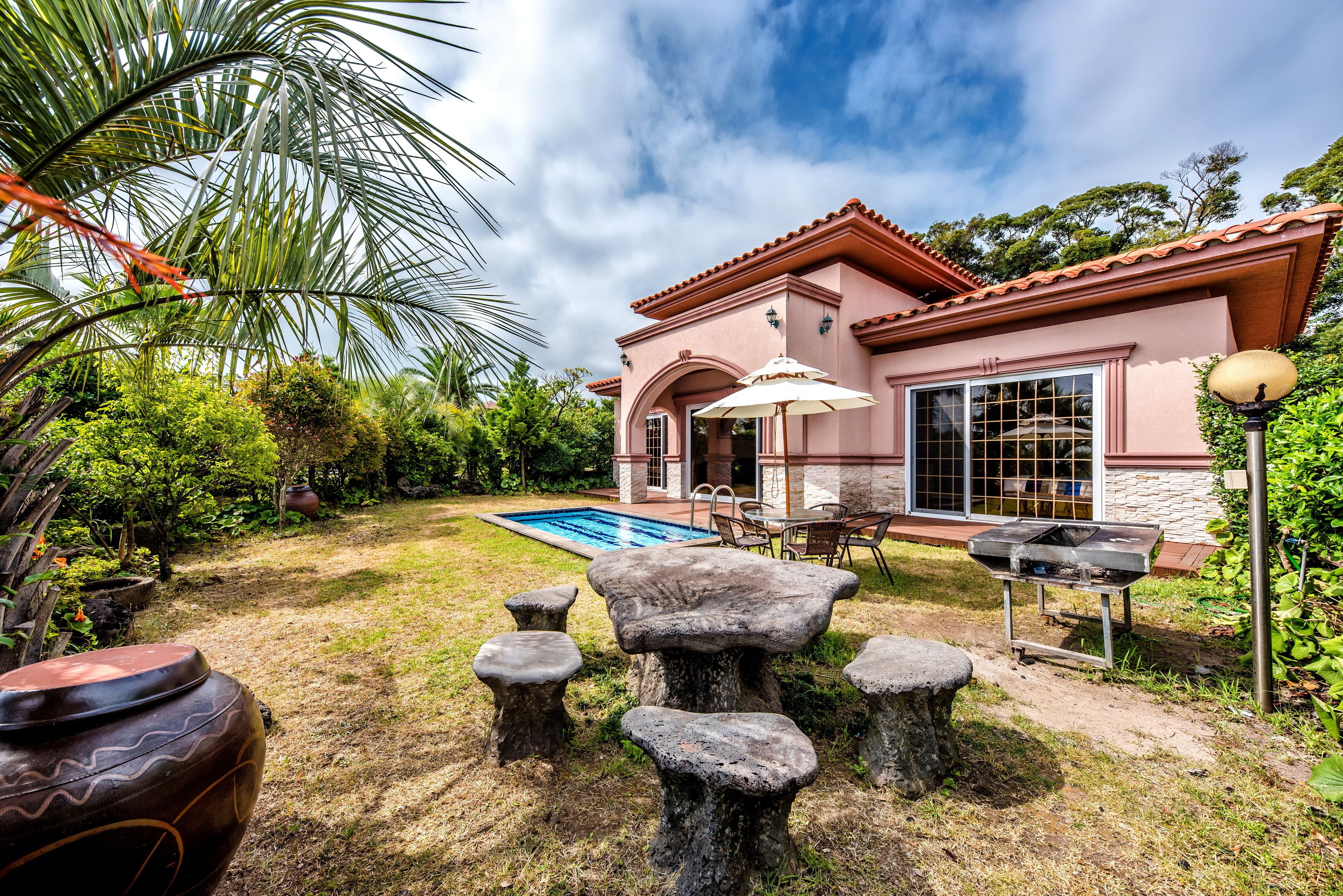 A house with a swimming pool, stone seating, and a barbecue area.
