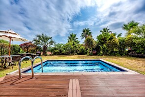 A wooden deck leading to a swimming pool surrounded by lush greenery and palm trees. - PalmValley Pool Villa Resort (Seogwipo)