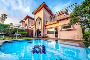 A swimming pool with a clear view of the surrounding architecture, including a two-story building with balconies and a patio area with outdoor furniture. - PalmValley Pool Villa Resort (Seogwipo)
