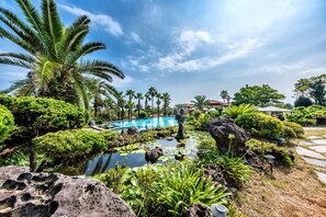 A tropical garden with a swimming pool, palm trees, and a statue. - PalmValley Pool Villa Resort (Seogwipo)