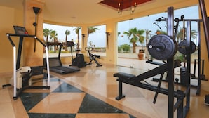A gym with cardio machines, weightlifting equipment, and a large window with a view of palm trees. - Amphoras Aqua Adults Friendly (Sharm El Sheikh)