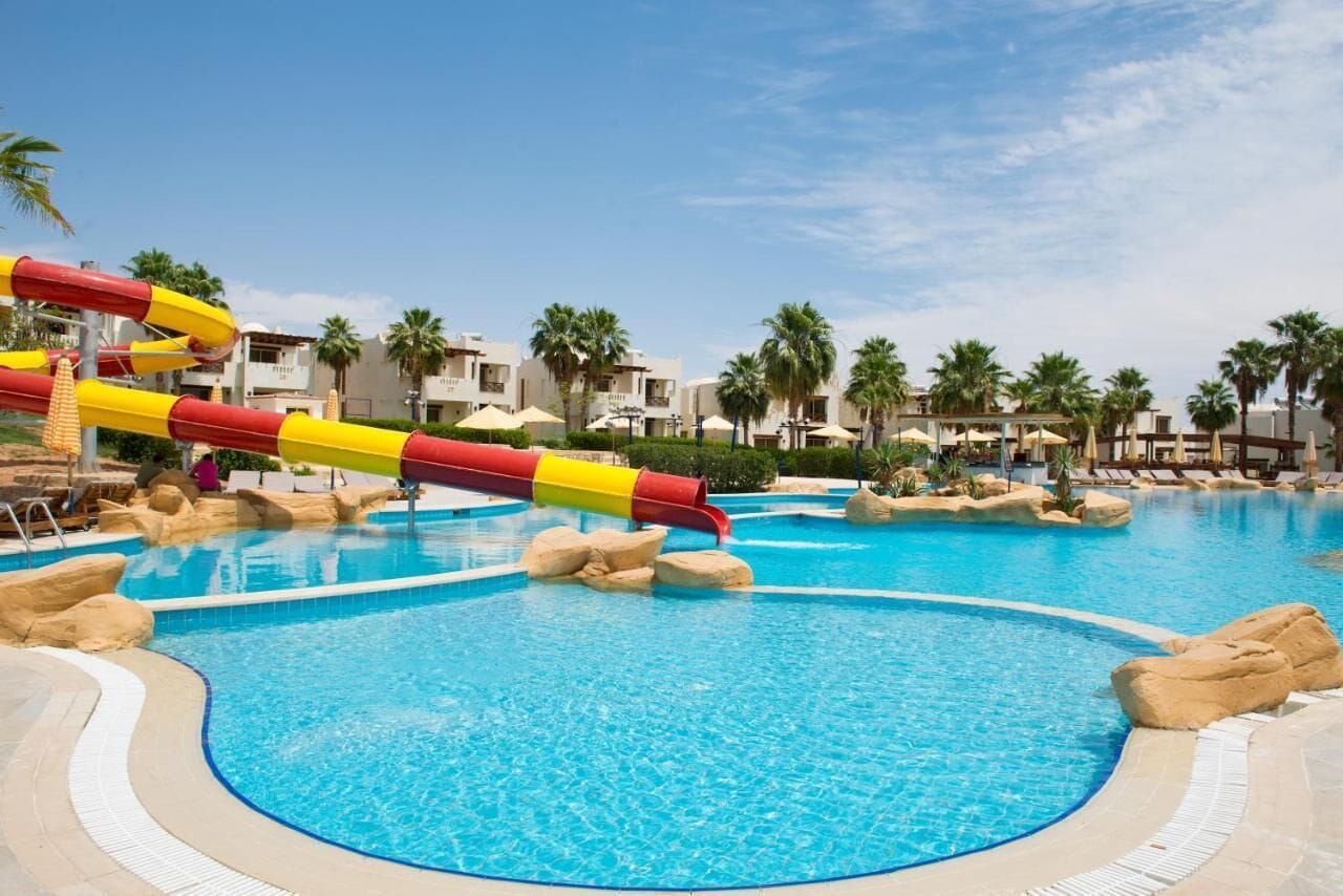 A swimming pool with a water slide, palm trees, and resort buildings.