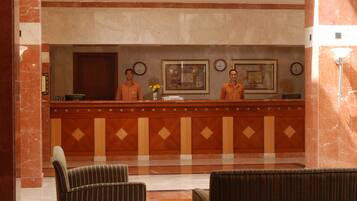 A reception desk with two staff members, a clock, and framed artwork on the wall.