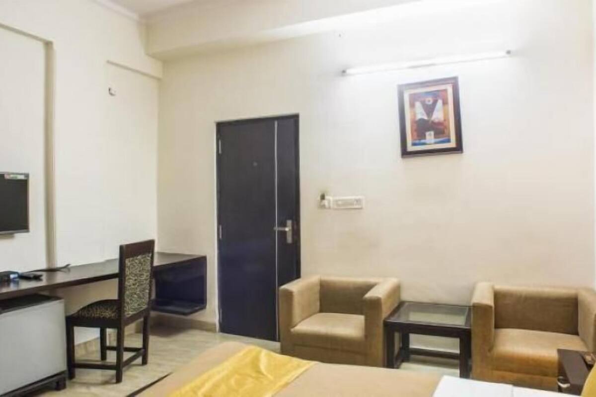 A hotel room with a desk, two armchairs, a bed, a TV, and a door.