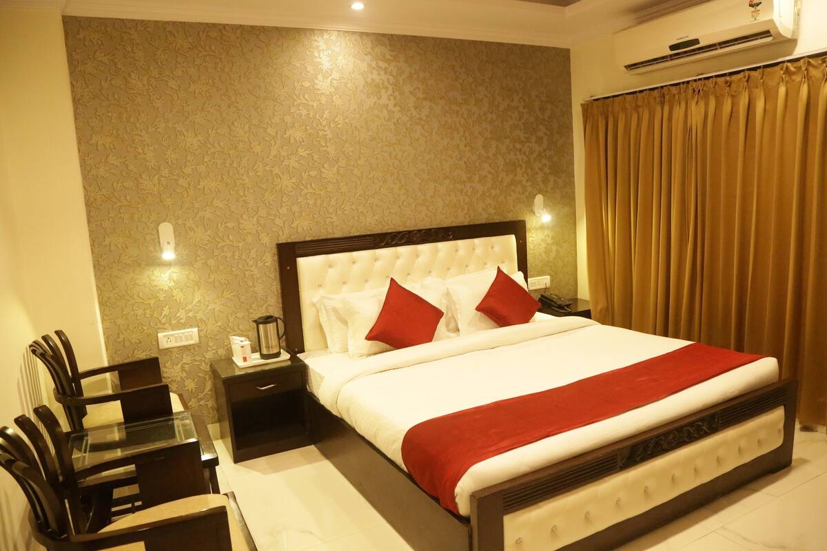 A neatly arranged hotel room with a large bed, a bedside table with a lamp, a chair, and a small table with a coffee maker.