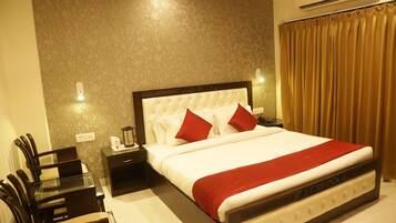 A neatly arranged hotel room with a large bed, a bedside table with a lamp, a chair, and a small table with a coffee maker.