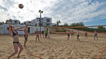 Un partido de voleibol de playa en una cancha arenosa, con una red en el centro, rodeado de jugadores.