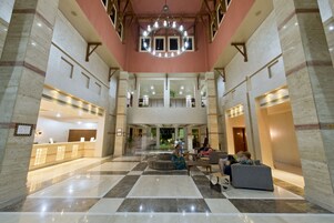 A spacious lobby with a checkered floor, a reception desk, seating areas, and a decorative ceiling light fixture.