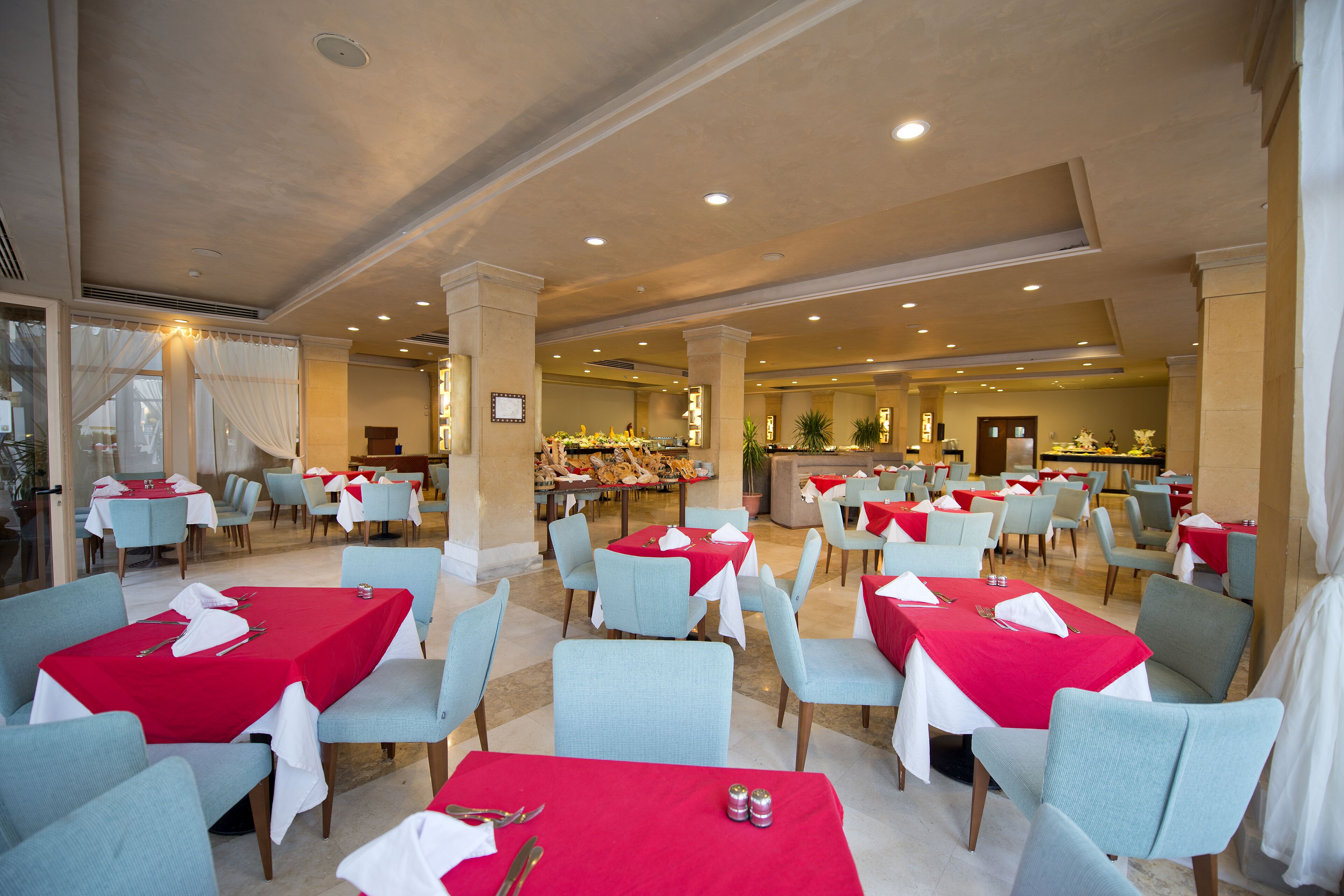 A spacious dining area with multiple tables and chairs, featuring a central buffet and a seating area with a view of the buffet.