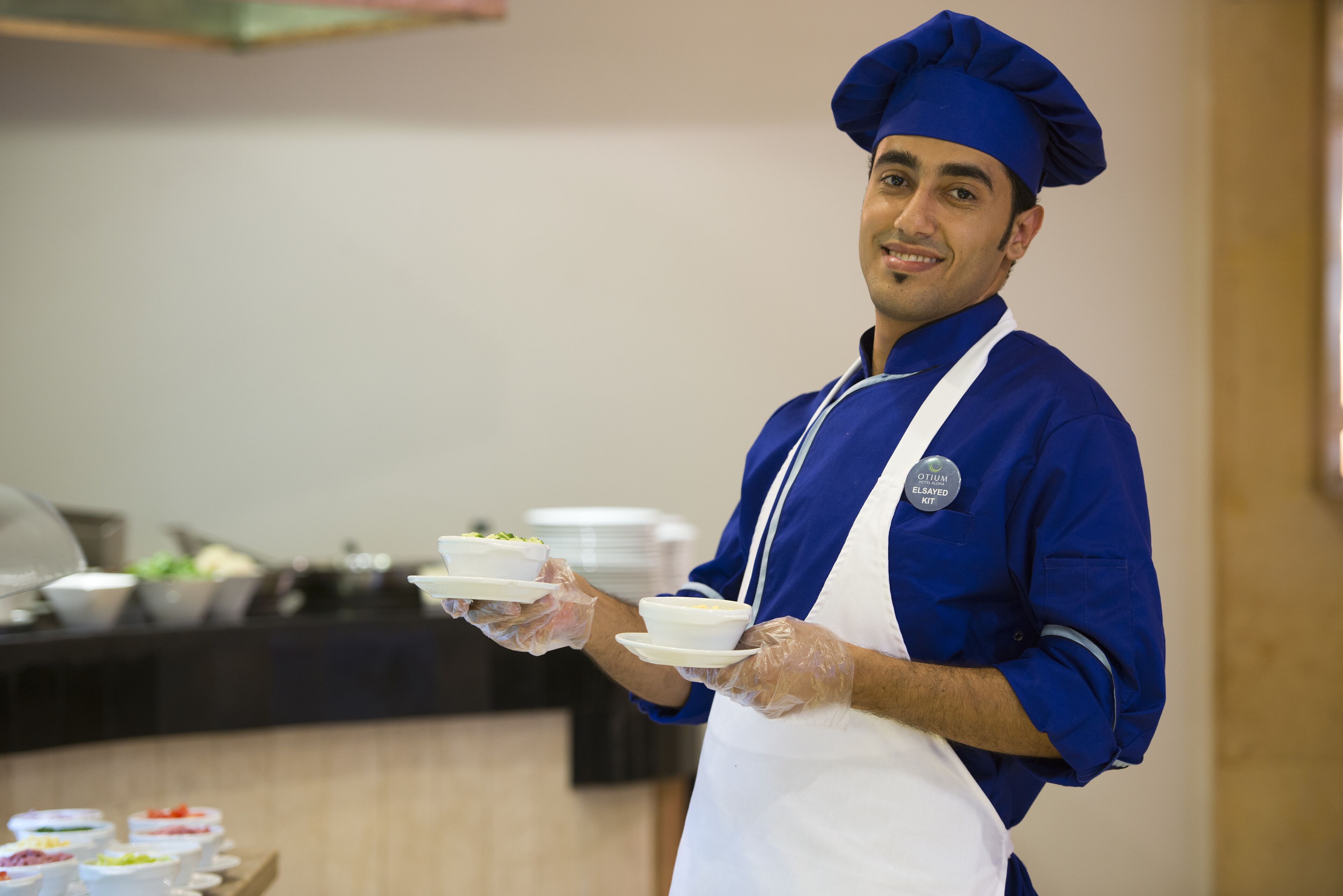 A person in a blue chef's uniform and hat holding plates with food.