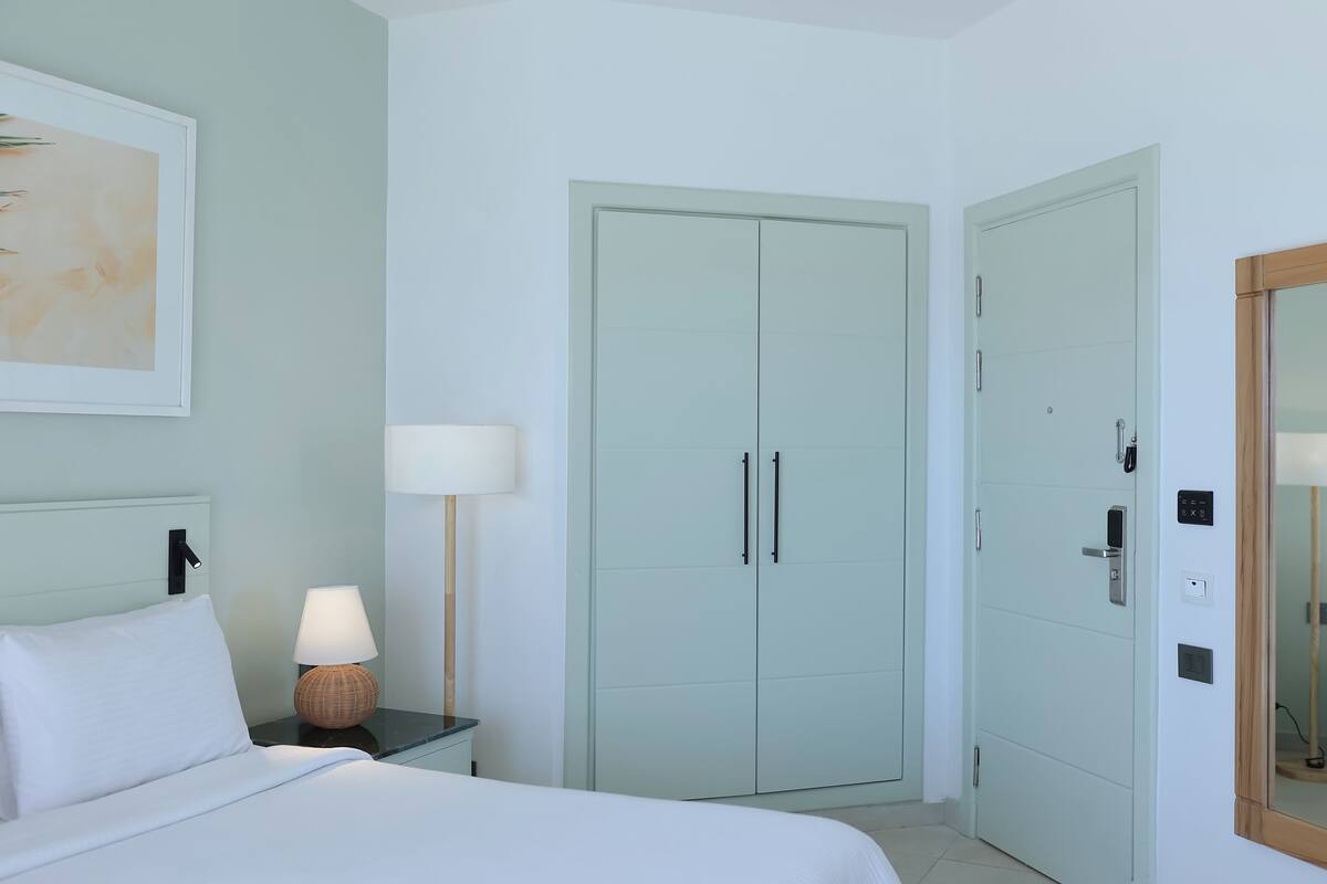 A bedroom with a bed, bedside lamp, wardrobe, and a mirror.