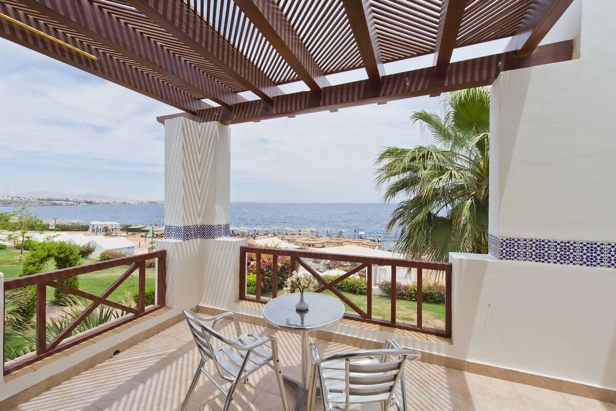 A balcony with a view of the sea, a table with chairs, and a decorative vase.