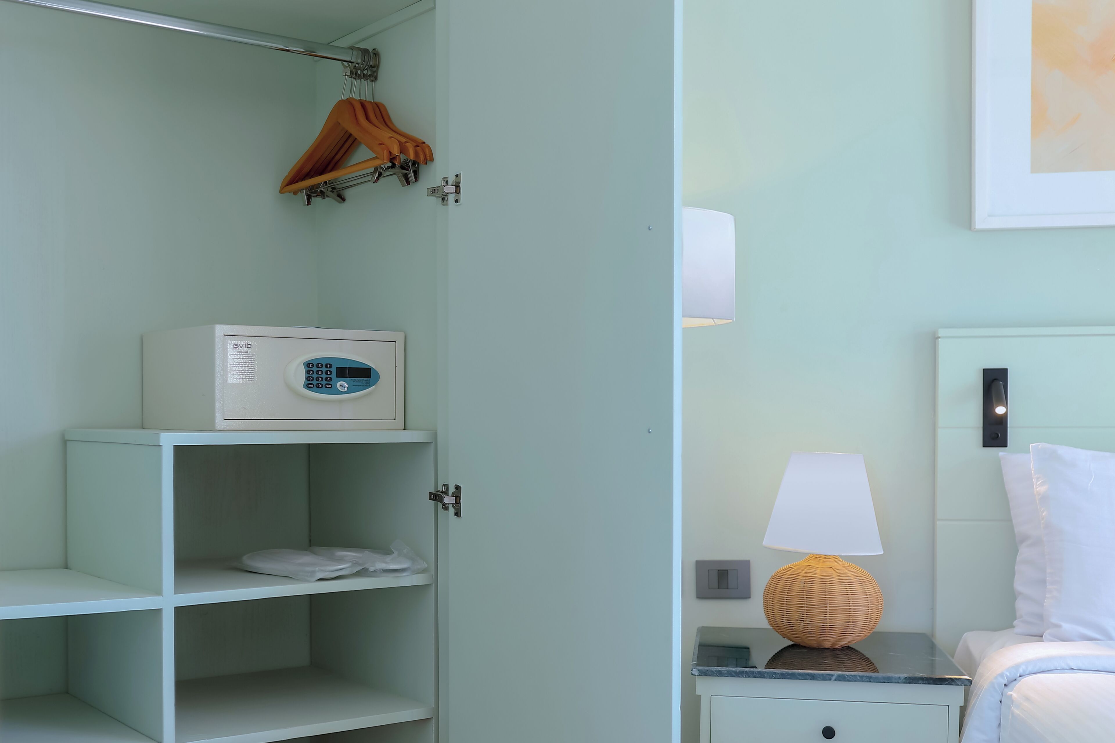 Une chambre avec une armoire blanche, une table de chevet avec une lampe et un lit avec du linge de lit blanc.
