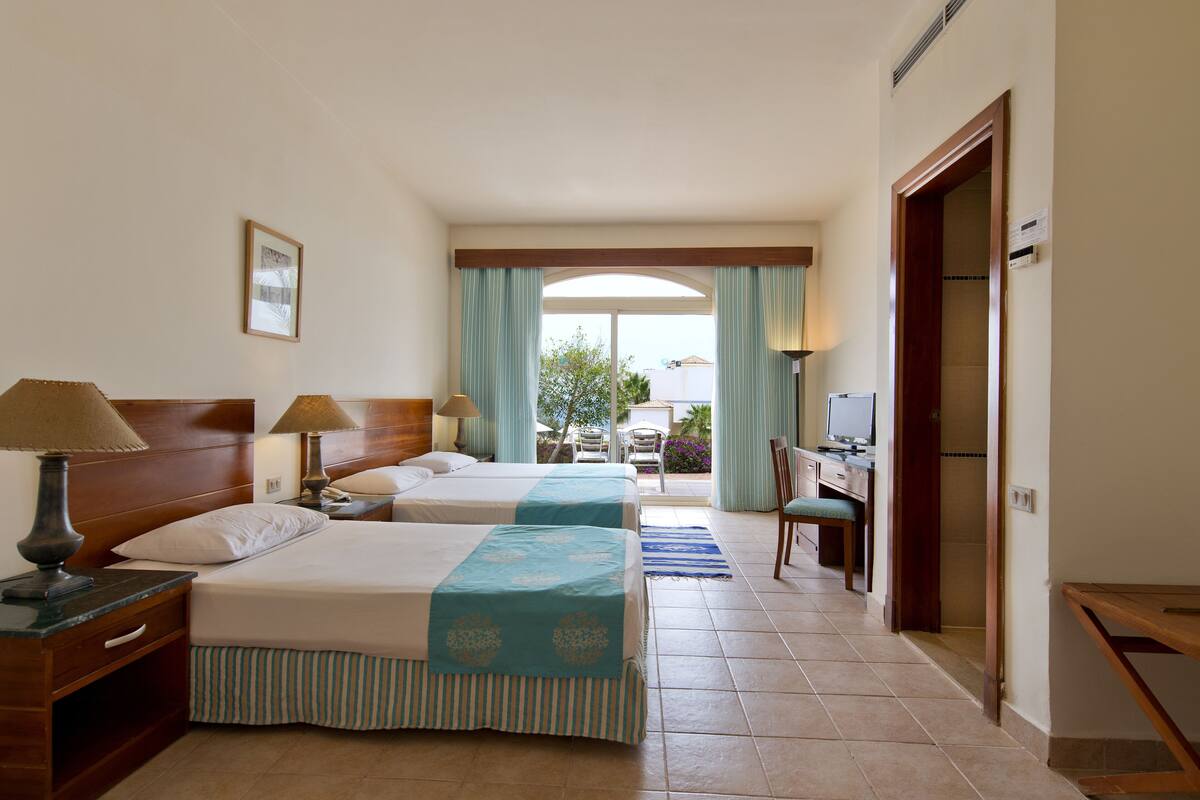 A hotel room with two beds, a desk, and a view of the outdoors.