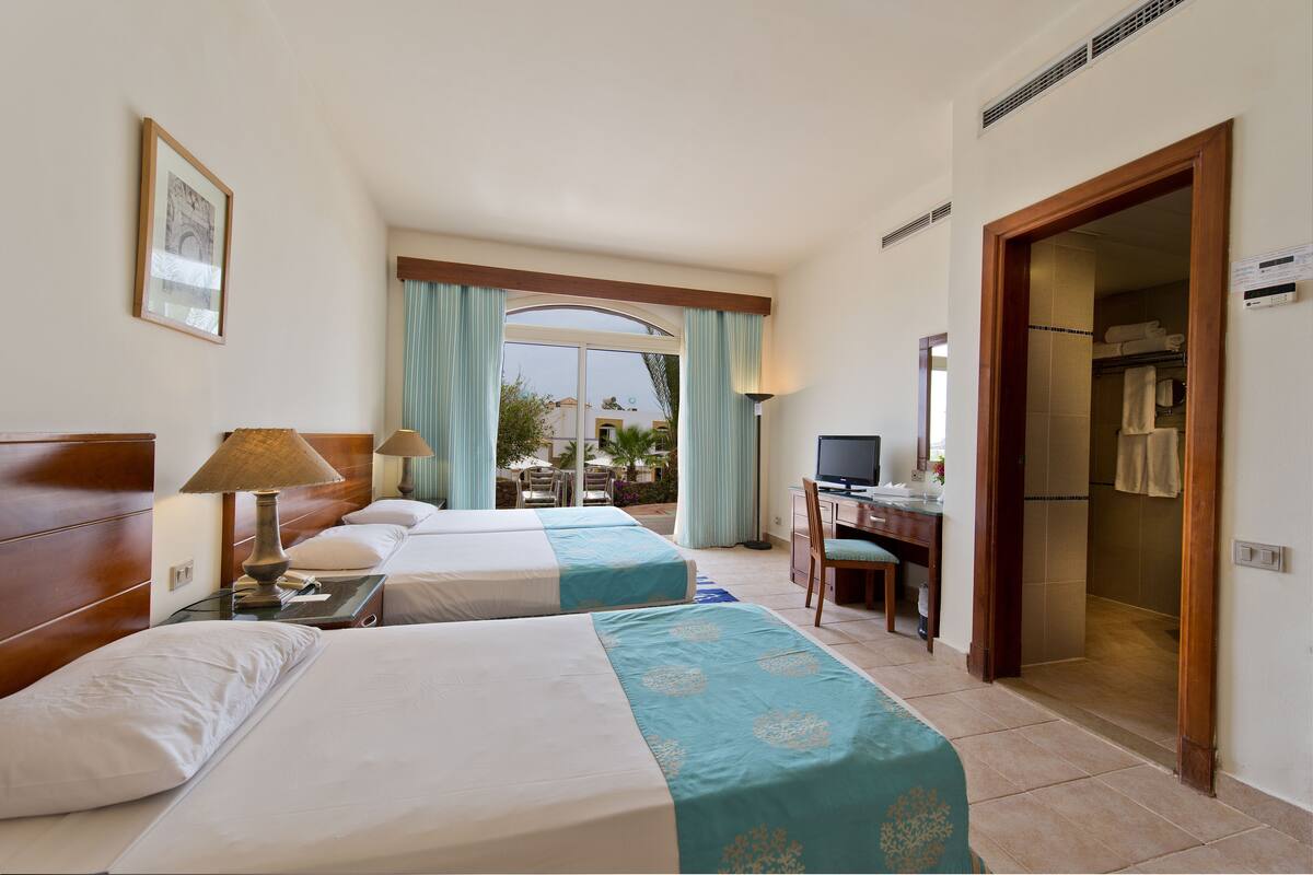 A hotel room with two beds, a desk with a chair, a television, and a bathroom visible through an open door.