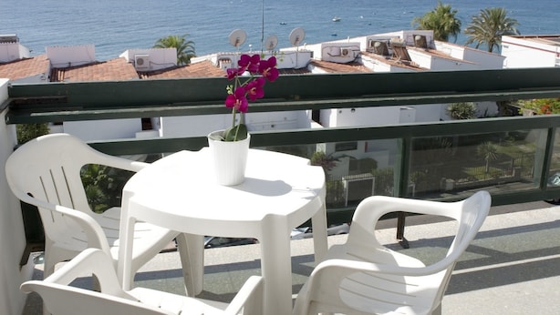 A balcony with white plastic chairs and a table, overlooking a coastal view with buildings and the sea. - Roca Verde (San Bartolomé de Tirajana)