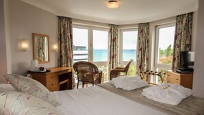 A hotel room with a bed, two chairs, a desk, a television, and large windows with curtains. - The Heritage Hotel (Torquay)